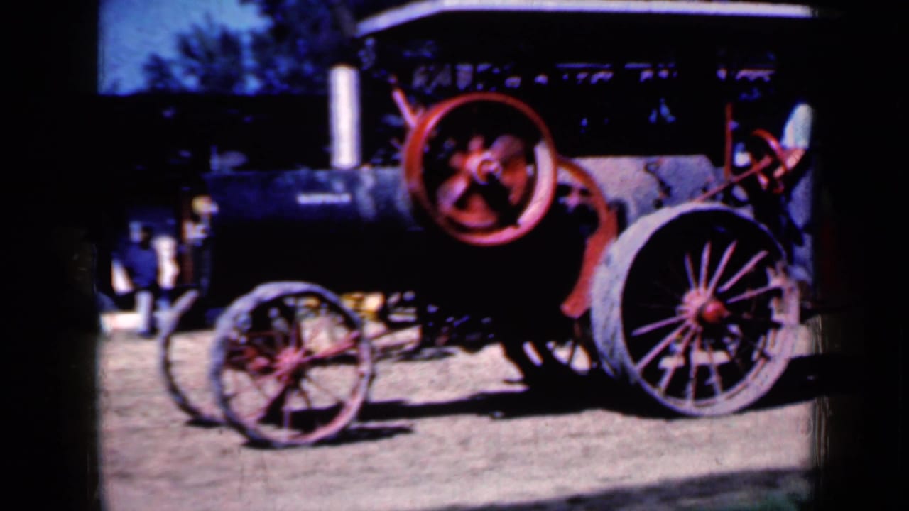 Steam traction engine with large red flywheel and spoked wheels on dirt ground.