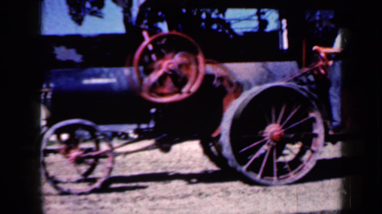 Close 8mm view of the antique steam tractor in Iowa, showing the black boiler, red flywheel, front wheel, and large spoked rear wheel.