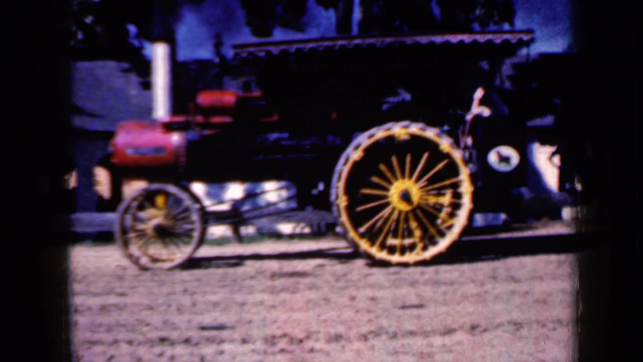 1959 Iowa frame showing a second vintage steam vehicle or tractor with a yellow spoked wheel, red machinery parts, and dark shade behind it.