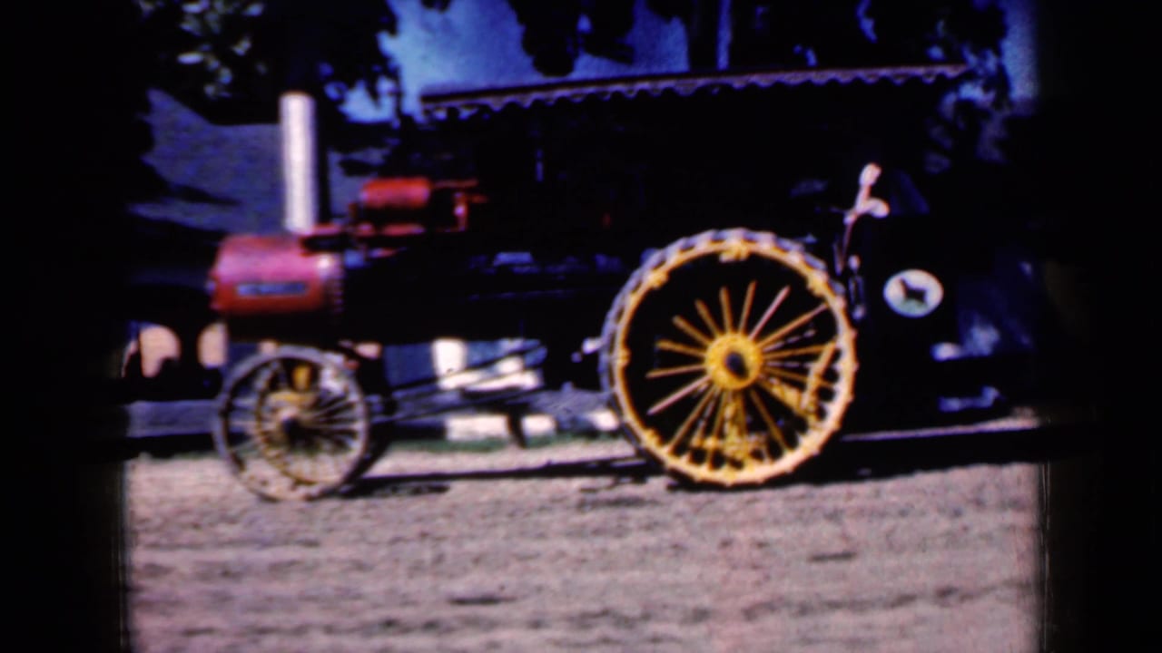 Steam tractor with red boiler and large yellow spoked rear wheel on dirt ground.