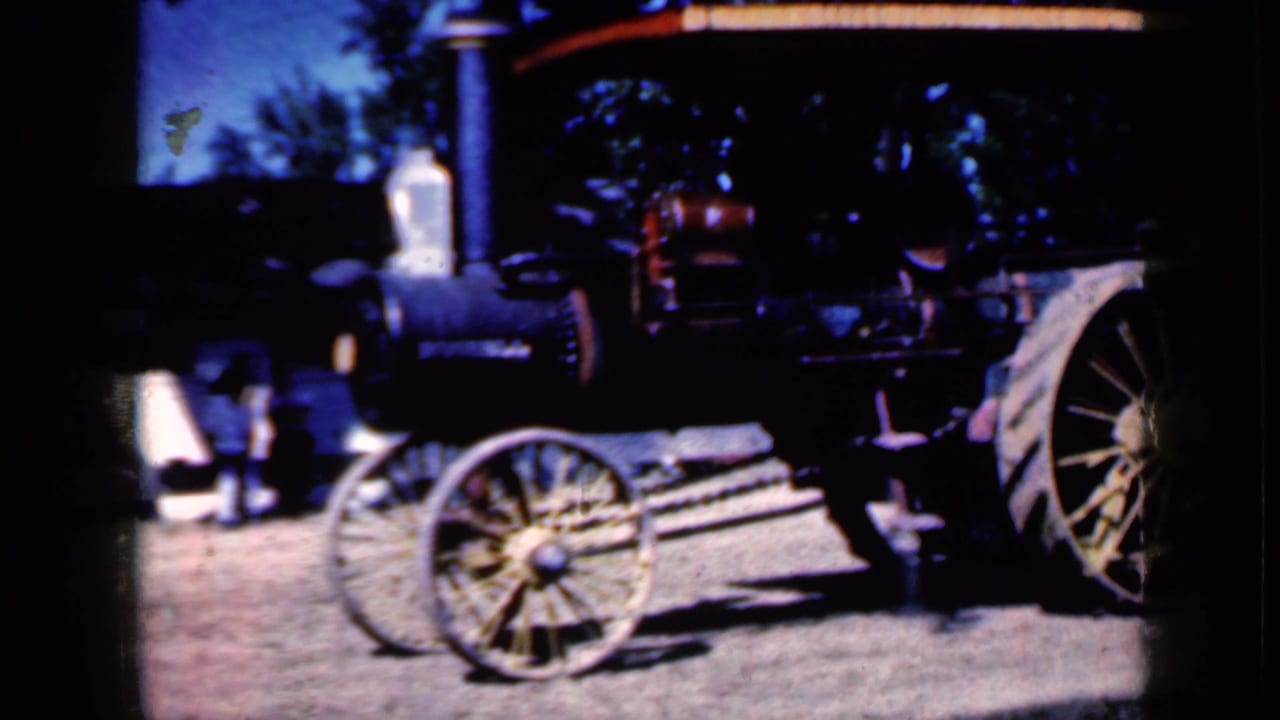 1959 Iowa home-movie frame showing the front portion of the steam tractor, including its smokestack, boiler face, small spoked wheel, linkage, and partial rear wheel.