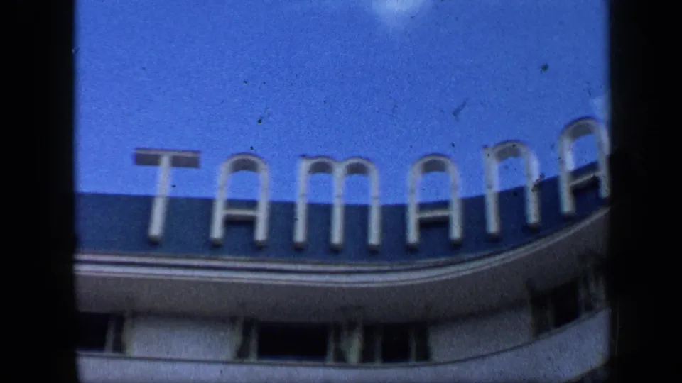 1959 Venezuela home-movie frame showing a curved exterior facade with large sign letters and blue sky.
