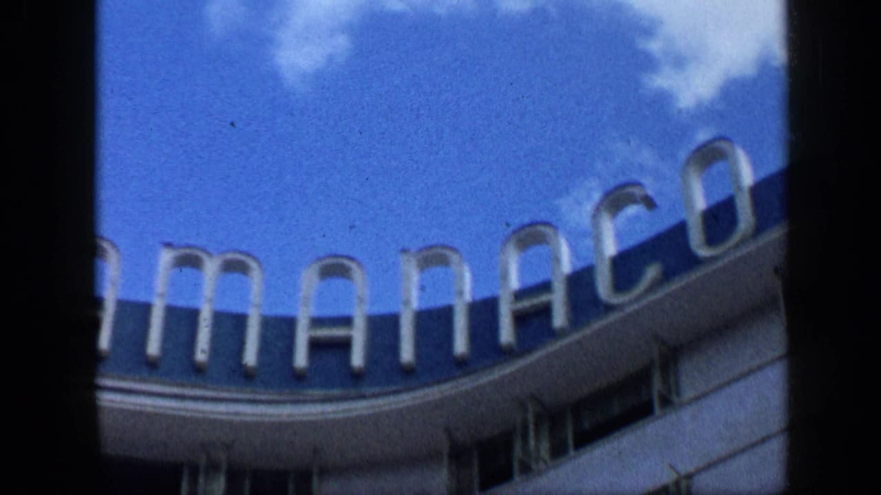 Curved sign and building edge under blue sky, framed by dark film borders.