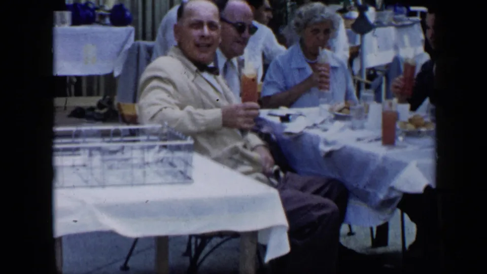 1959 Venezuela dining scene with older adults at a white-tablecloth outdoor table, drinks, plates, and period clothing visible.