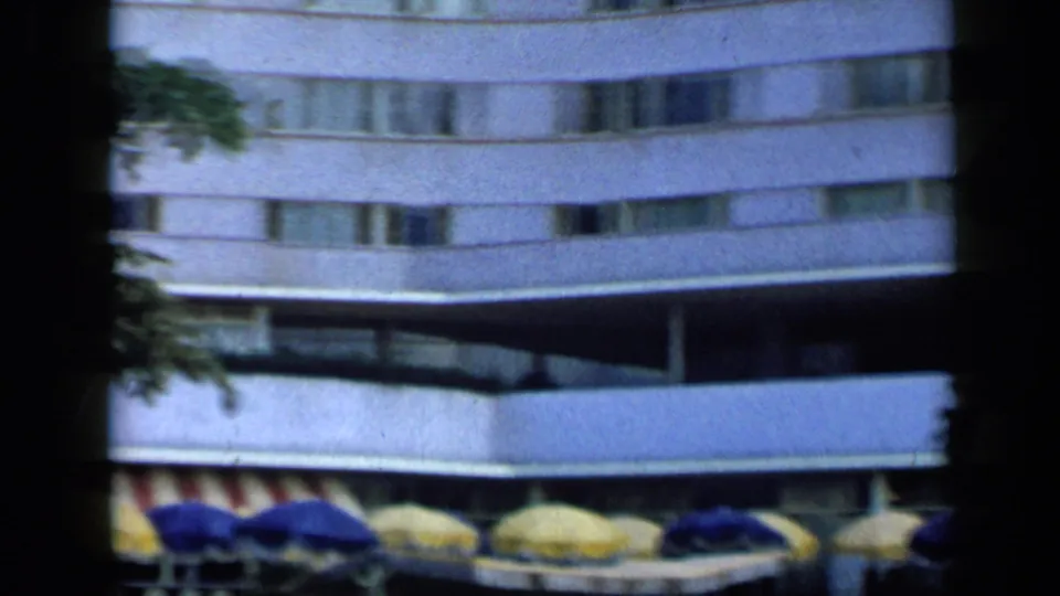 Modernist hotel facade in Venezuela, 1959, with striped awnings and blue-yellow umbrellas along the poolside.