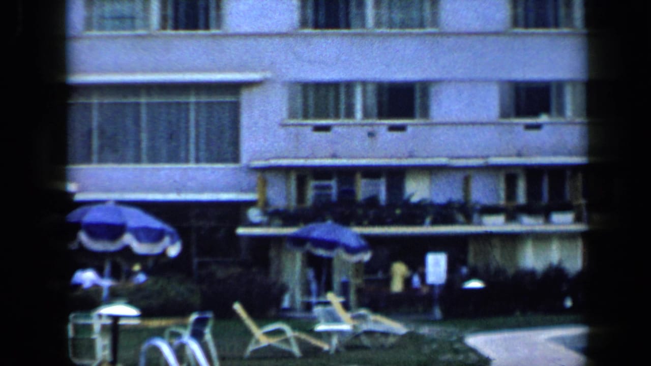 1959 Venezuela resort poolside view with lounge chairs, umbrellas, palm tree, and distant guests near a hotel facade.