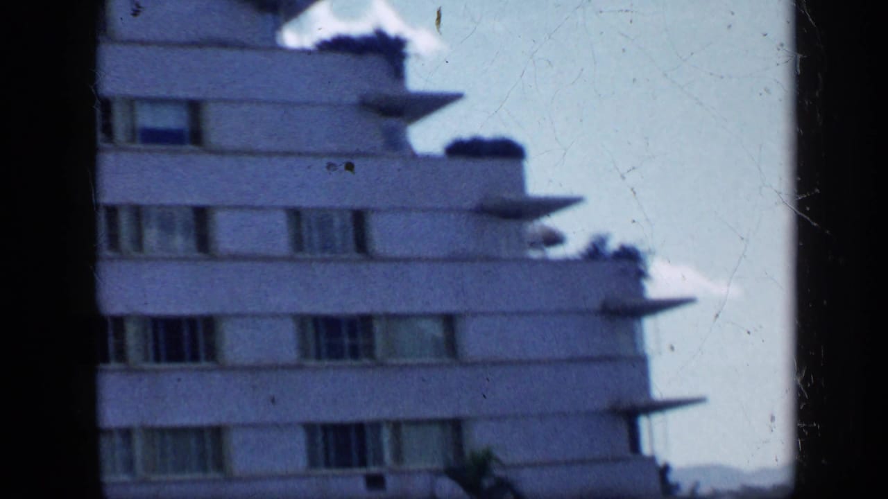 1959 Venezuela 8mm view of a white modernist apartment building, seen from below with horizontal windows and tiered balcony edges.