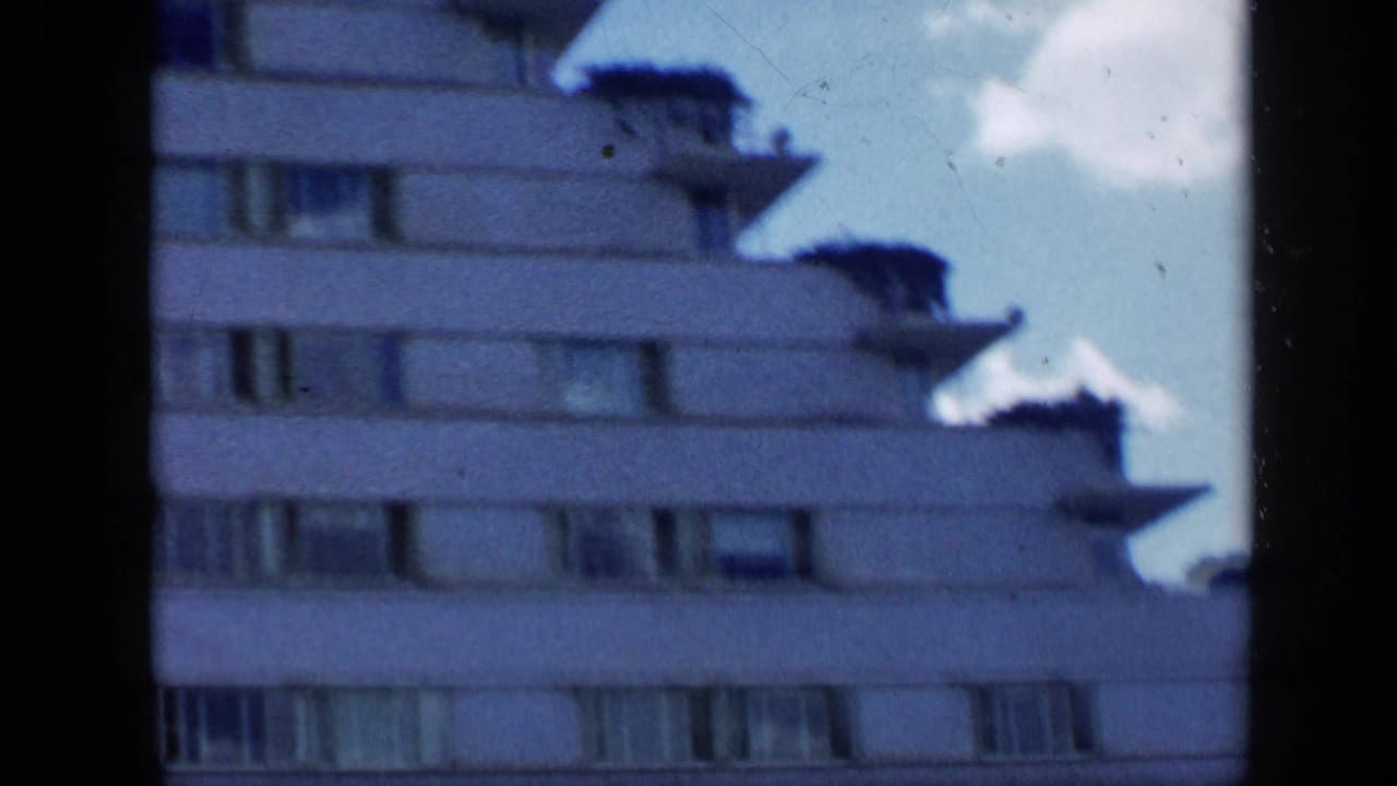 Upper stories of a white apartment building with tiered balconies and dark film borders.
