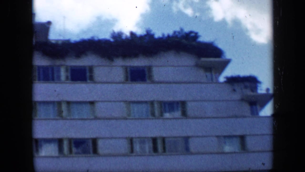 1959 Venezuela 8mm view of a residential high-rise facade, with planted roofline areas, window rows, and a pale sky behind it.