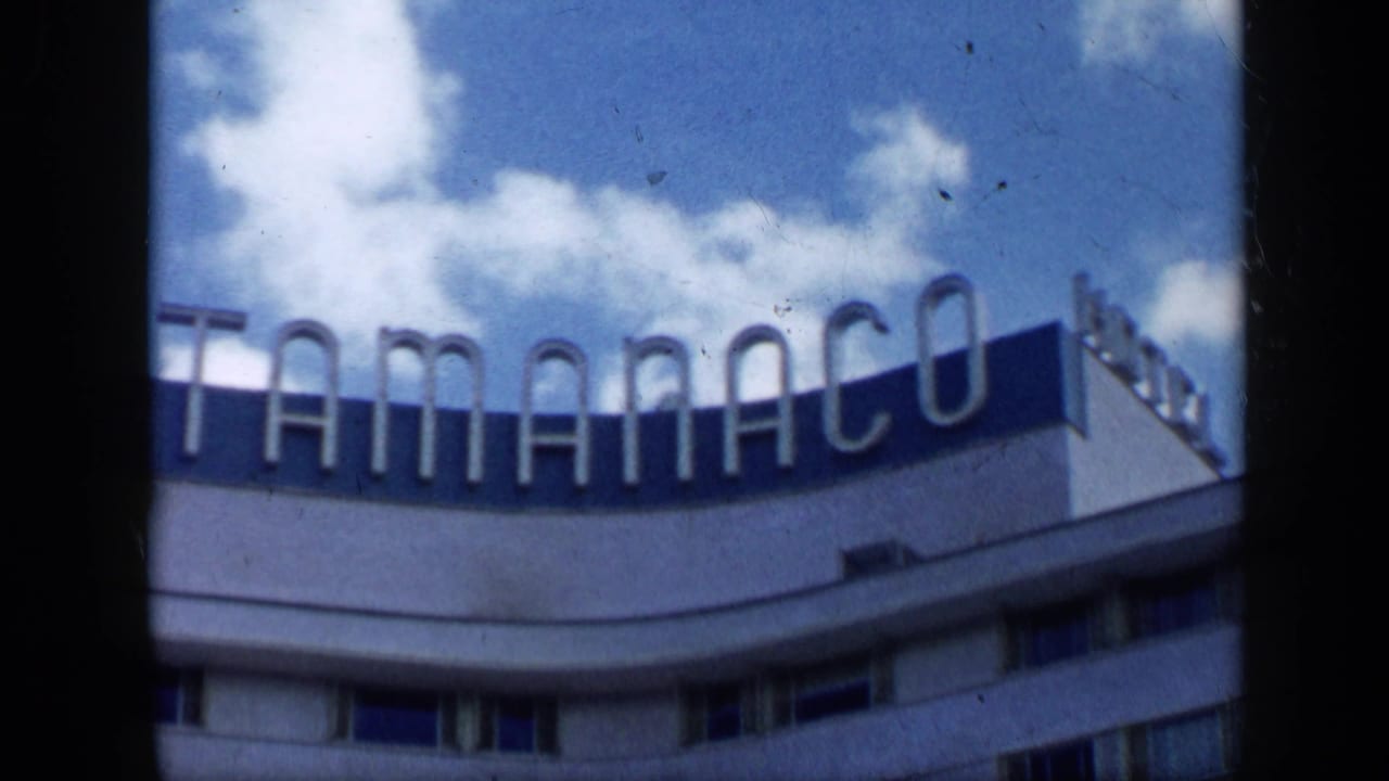 1959 Venezuela 8mm frame showing the TAMANACO rooftop sign on the hotel against scattered clouds.