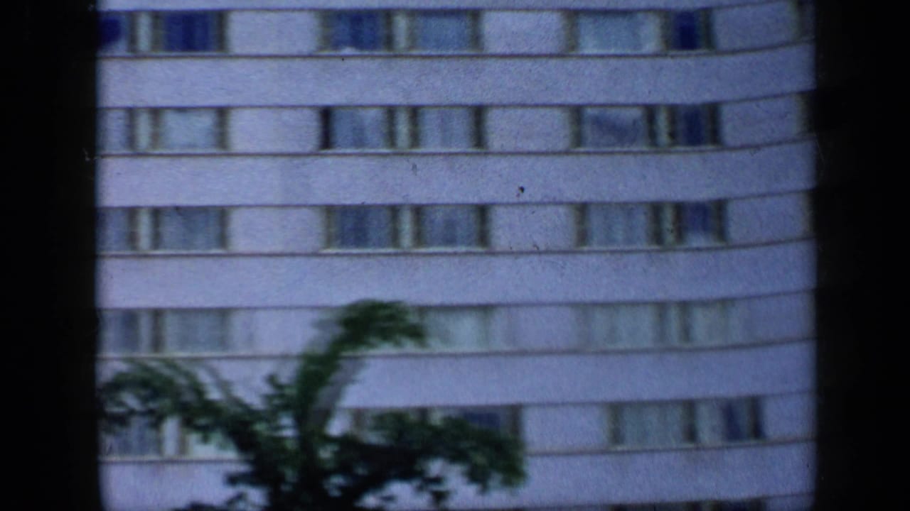 White multi-story building with rows of windows seen through dark film-frame edges.