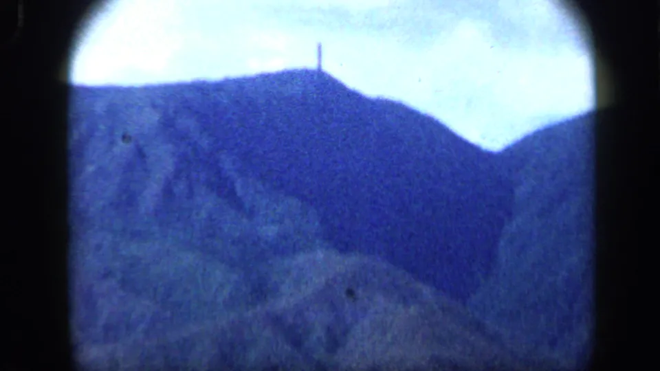 Grainy 1959 8mm frame from Venezuela showing a mountain ridge and a small vertical monument silhouetted near the top.