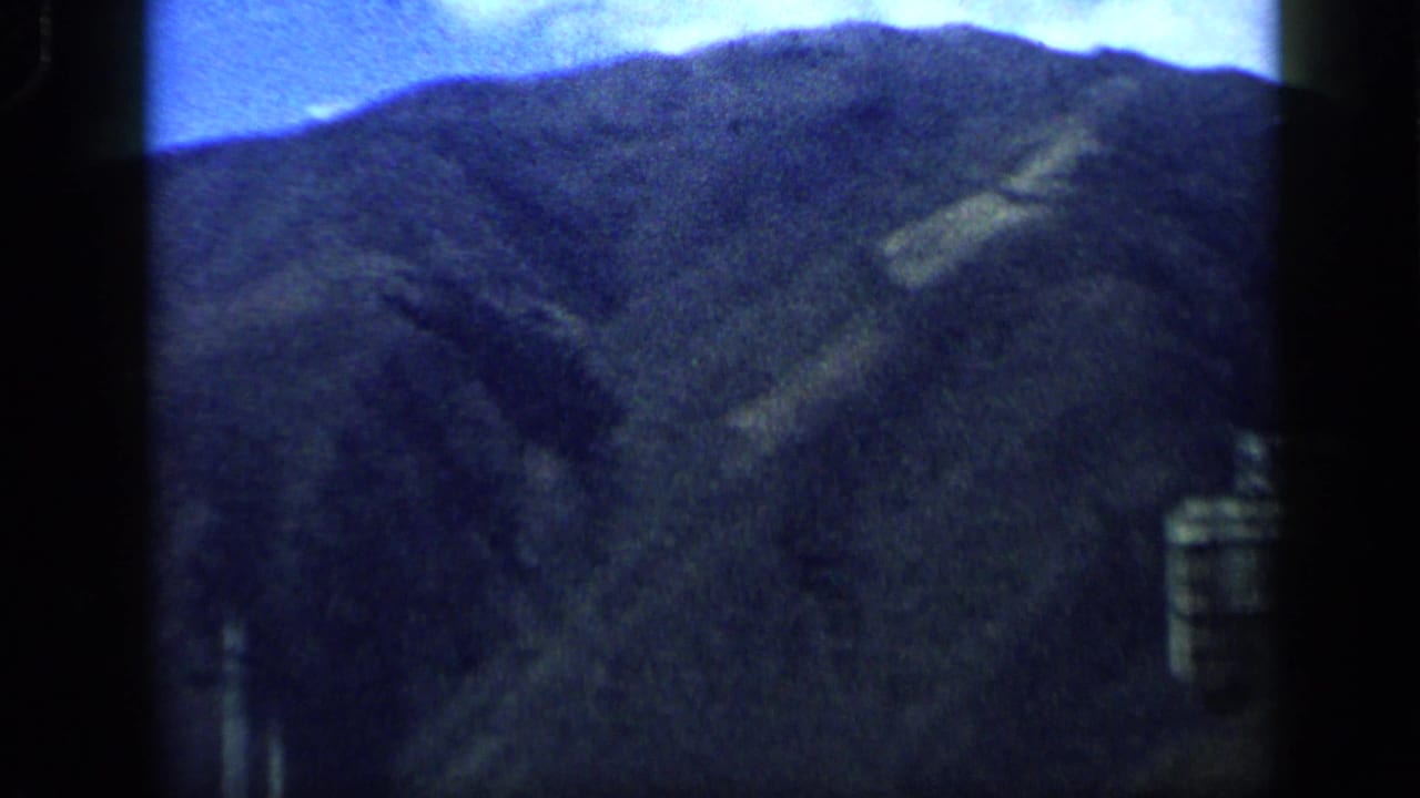 1959 Venezuela 8mm frame with a steep vegetated mountain ridge beneath a bright sky after the pan leaves the sign.