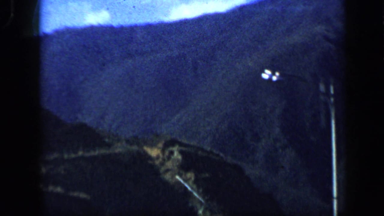 1959 Venezuela 8mm frame showing dark mountain ridges and small bright lights or a distant hillside sign.