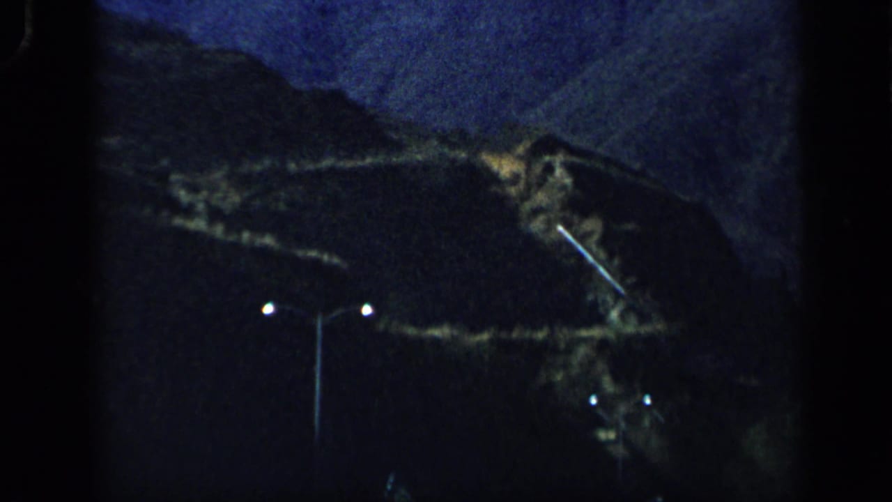 1959 Venezuela 8mm frame showing a dim mountain slope, small lights, and a vertical pole near the end of the pan.