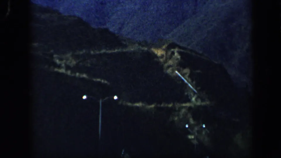 1959 Venezuela 8mm frame showing a dim mountain slope, small lights, and a vertical pole near the end of the pan.