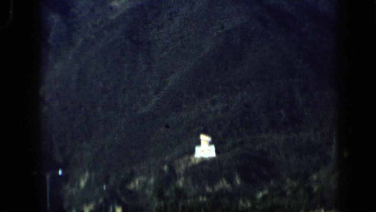 1959 Venezuela 8mm frame showing a dark hillside and a small illuminated sign-like structure near a nighttime road.