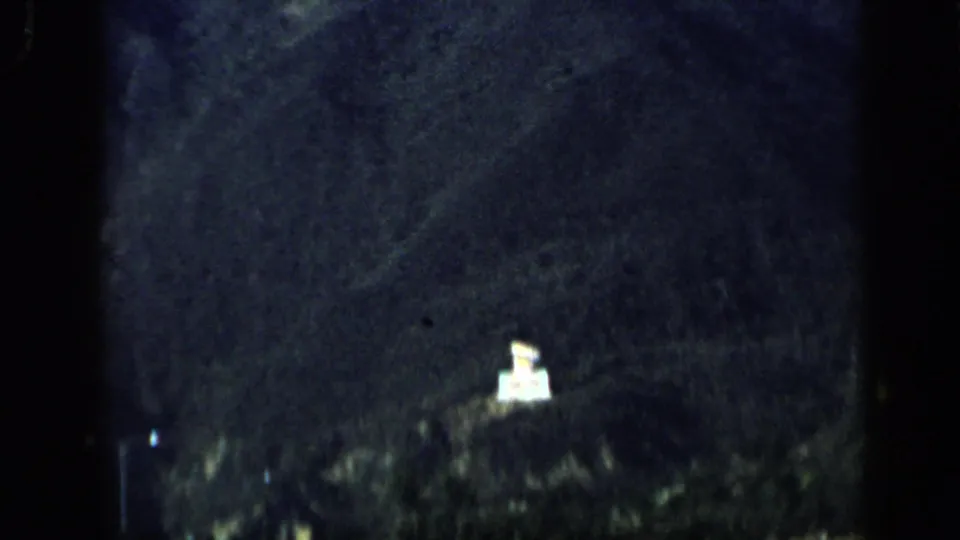 1959 Venezuela 8mm frame showing a dark hillside and a small illuminated sign-like structure near a nighttime road.