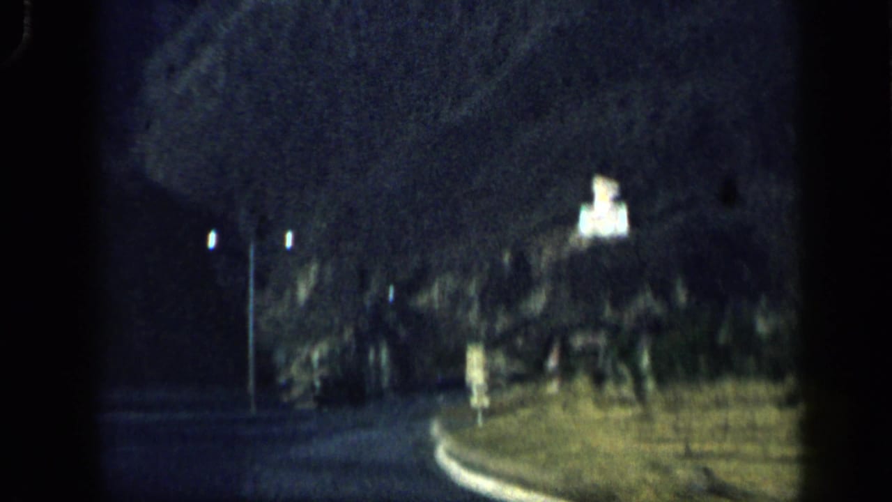 Curving road at night with streetlights and an illuminated hillside feature.