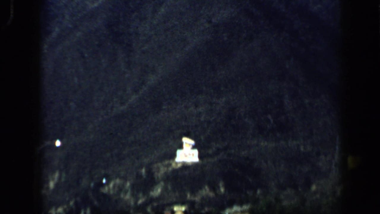 1959 Venezuela 8mm view of a shadowed hillside, faint roadside lights, and a bright sign-like object at night.