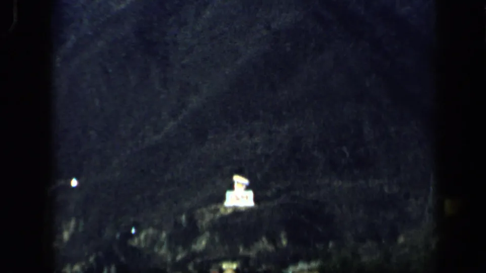 1959 Venezuela 8mm view of a shadowed hillside, faint roadside lights, and a bright sign-like object at night.