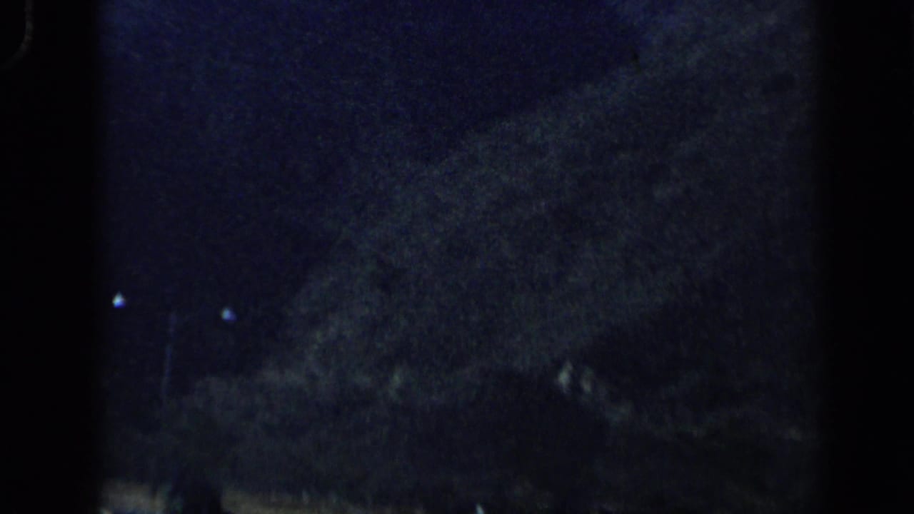 Shadowed Venezuelan mountain terrain passes through the 8mm frame, with low exposure and faint light spots in the distance.