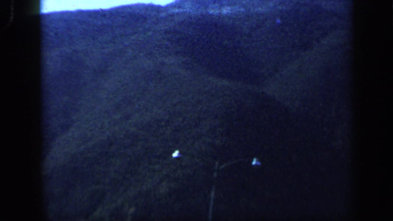 A soft, blue-toned 8mm view of Venezuelan mountainsides and dark foreground landscape from a moving vehicle.