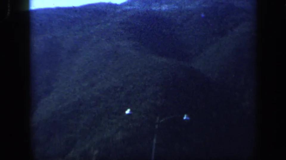 A soft, blue-toned 8mm view of Venezuelan mountainsides and dark foreground landscape from a moving vehicle.