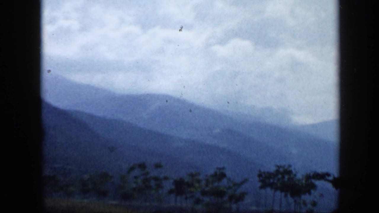 Layered mountains seen through a dark vehicle window under cloudy sky.