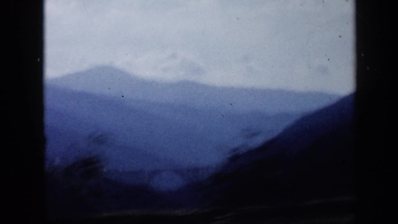 A soft blue mountain ridge in Venezuela is seen from inside a moving vehicle, with dark window borders dominating the frame.