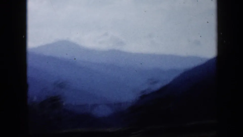 A soft blue mountain ridge in Venezuela is seen from inside a moving vehicle, with dark window borders dominating the frame.