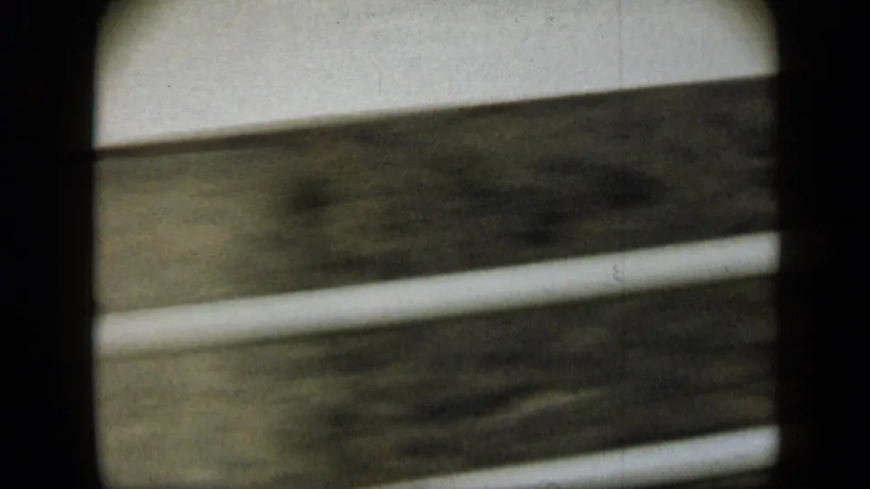 Soft, grainy 1959 Venezuela road-trip frame showing a close roadside barrier through a moving vehicle window.