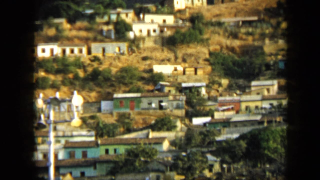 Hillside town in Venezuela, filmed from a distance on 8mm, with modest buildings scattered across steep terrain.