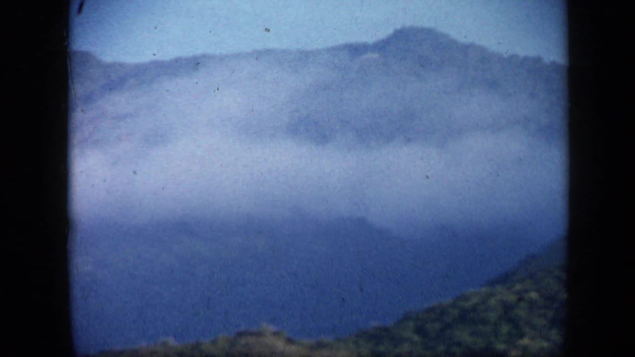 1959 8mm Venezuelan mountain vista with hazy blue ridges, mist, and a dark foreground slope.