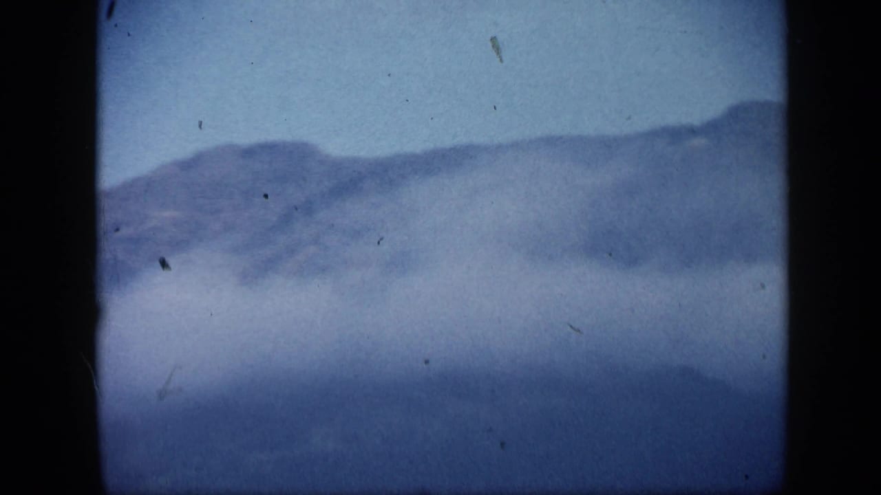 1959 Venezuela 8mm frame showing a distant mountain slope with low cloud or smoke and soft blue color fading.
