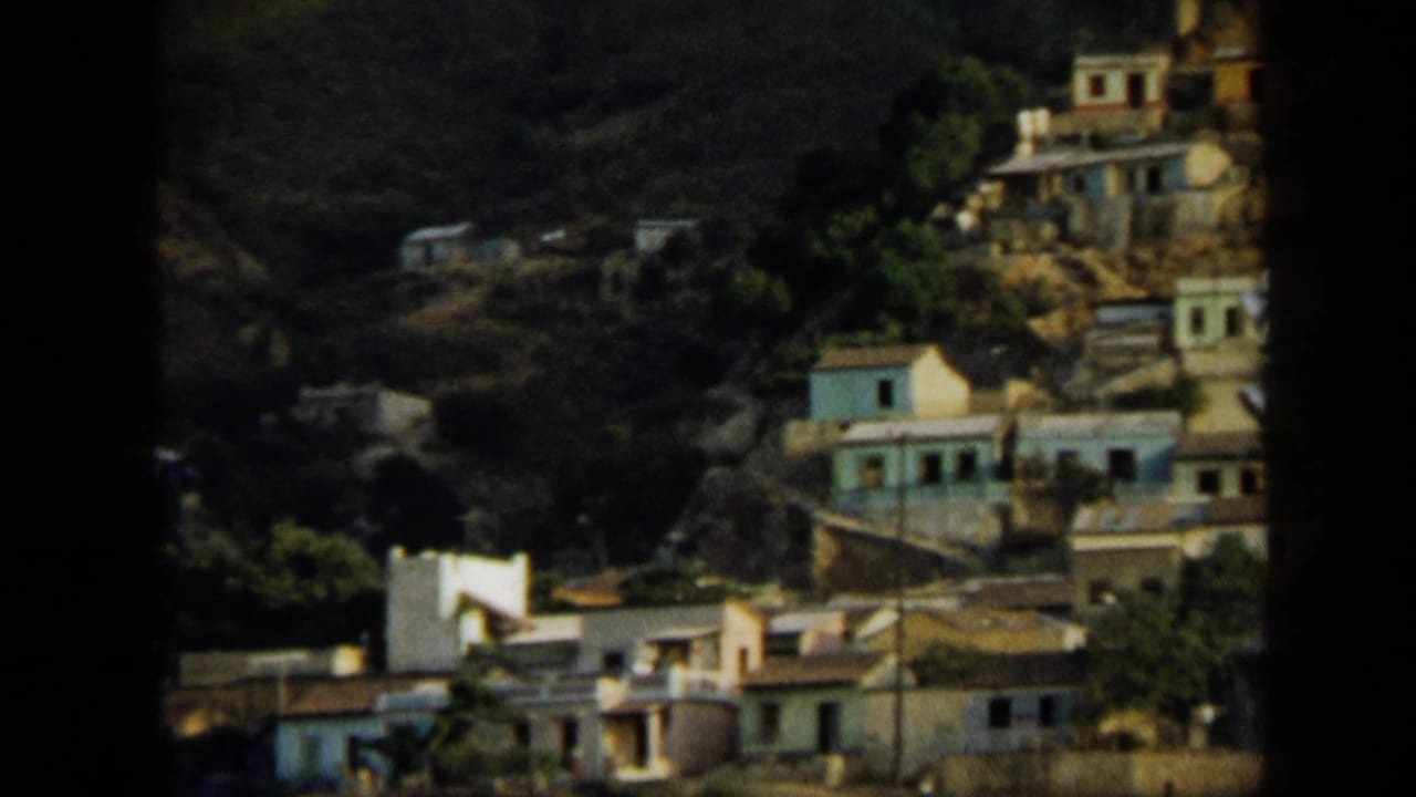 1959 Venezuela 8mm view of hillside homes with pale and blue walls among green foliage on steep terrain.