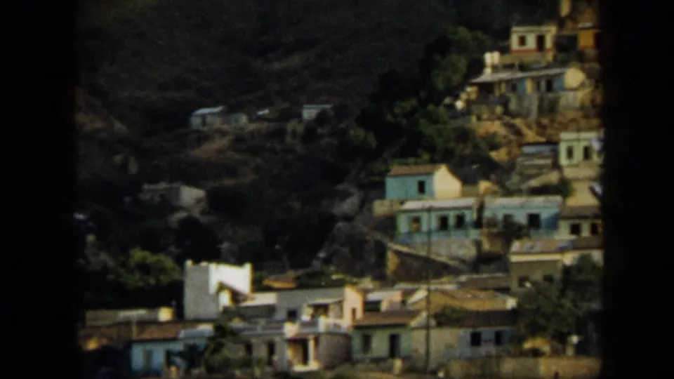 1959 Venezuela 8mm view of hillside homes with pale and blue walls among green foliage on steep terrain.