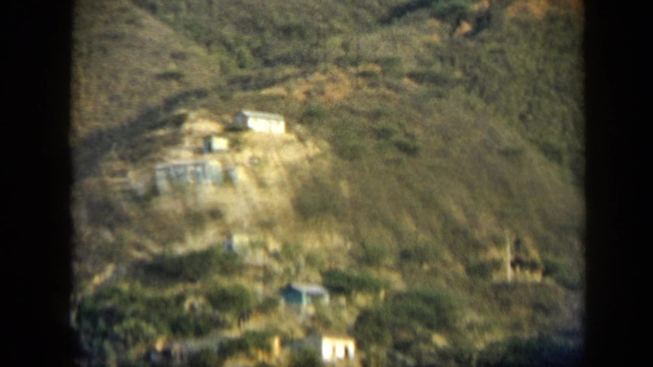 Distant hillside structures in Venezuela, filmed in 1959 with soft 8mm focus and dry mountain terrain.
