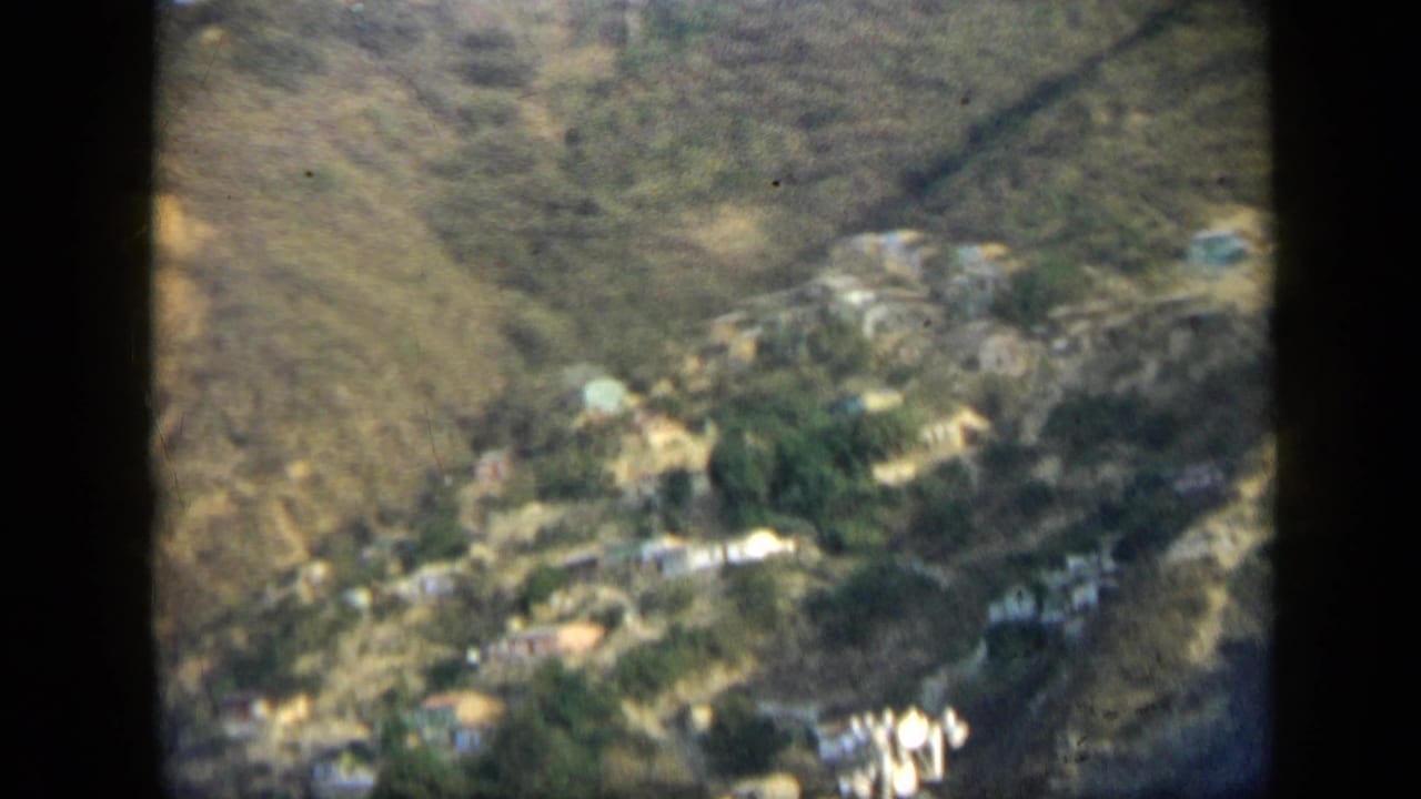 Wide 1959 Venezuela view of a hillside settlement with scattered homes, vegetation, and dry mountain terrain.