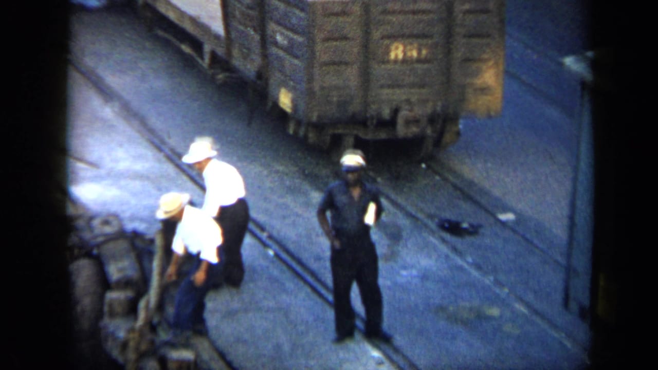 1959 Venezuela rail-yard view with workers in white and dark clothing tending freight cars and trackside equipment.