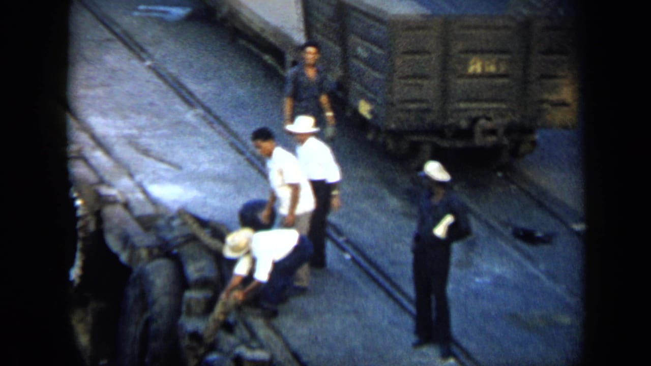 Rail-yard workers in white hats and dark uniforms tend equipment near freight cars in 1959 Venezuela.