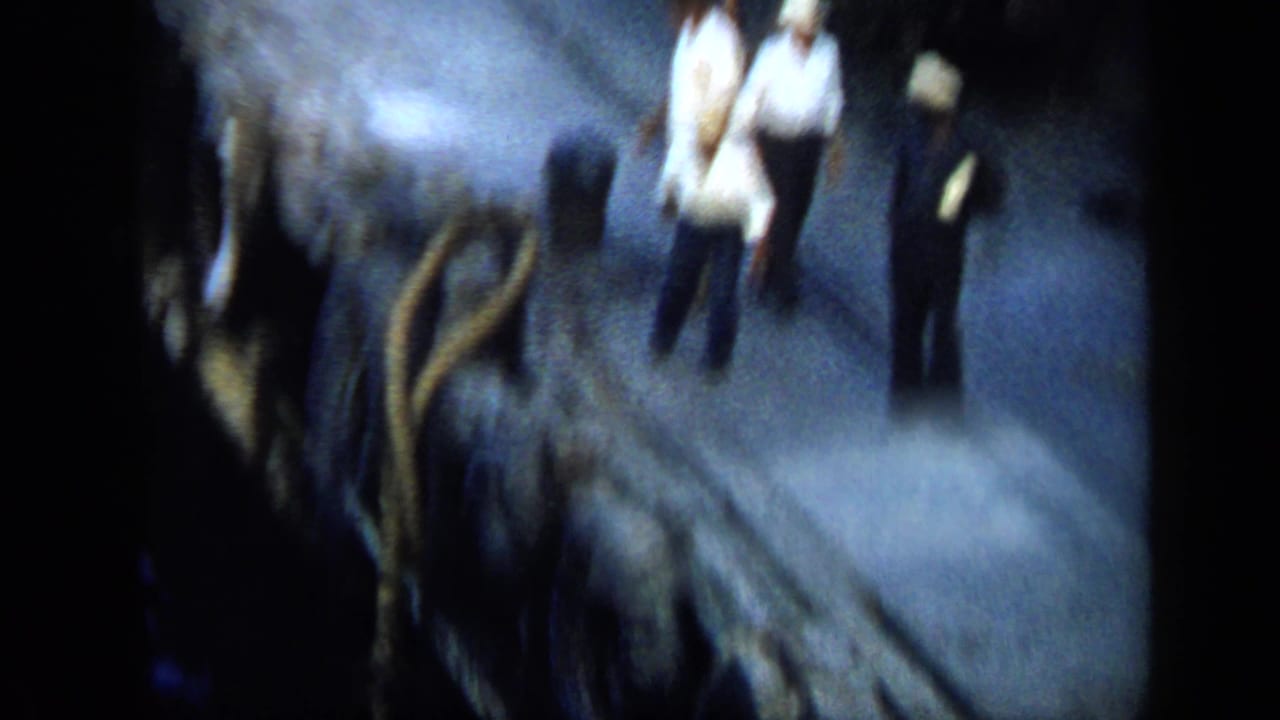 Venezuela 1959 8mm frame showing men on a dark dock near ropes or gear, softened by motion blur and low light.