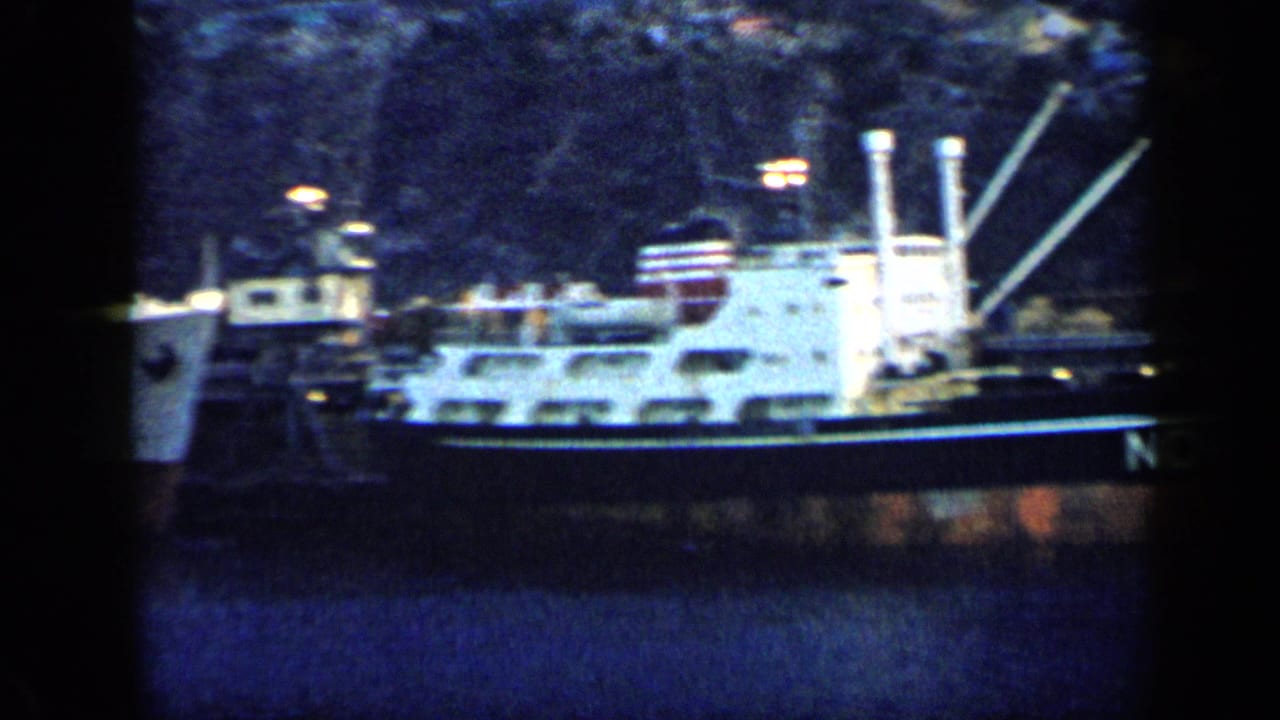Venezuela 1959 home-movie frame showing a side view of a docked cargo ship with white superstructure and rigging.