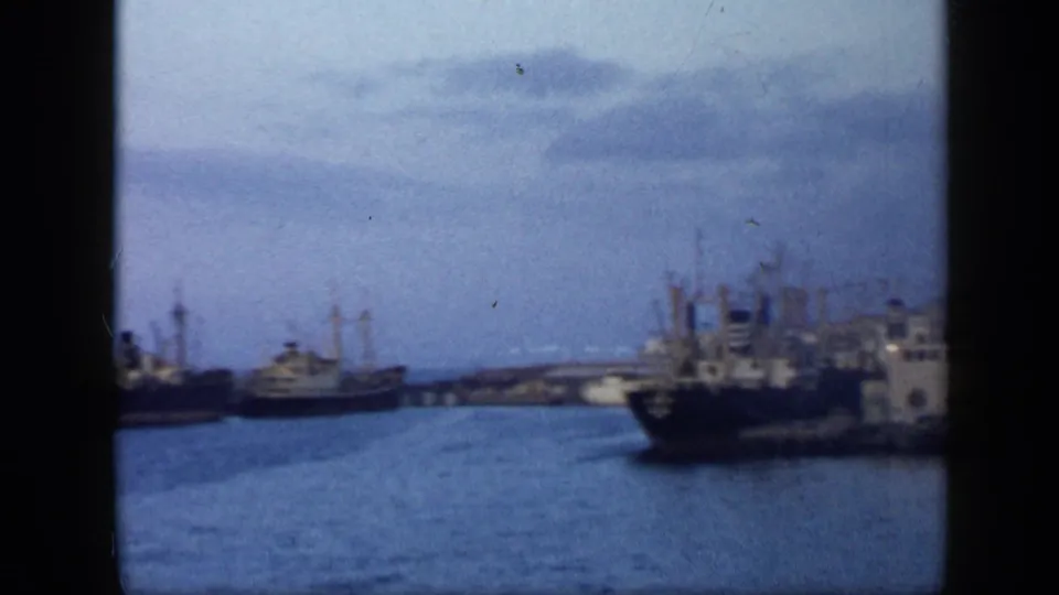 1959 Venezuela port view with cargo ships moored along the waterfront, crane masts, industrial buildings, and calm harbor water.