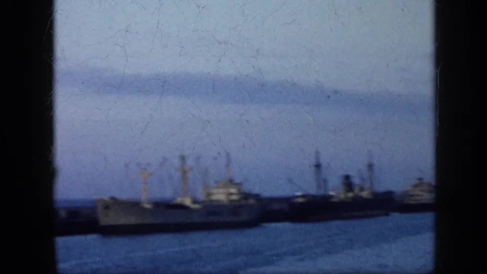 1959 Venezuela harbor frame showing multiple cargo vessels at dock, crane masts, industrial waterfront forms, and visible 8mm scratches.