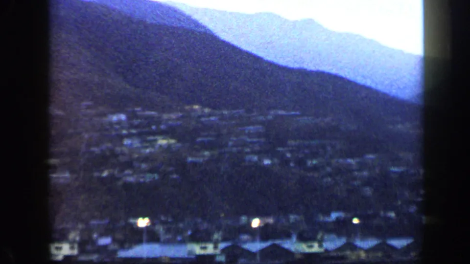 1959 Venezuela home-movie view looking over a hillside town at dusk, with layered blue mountains and small lights below.
