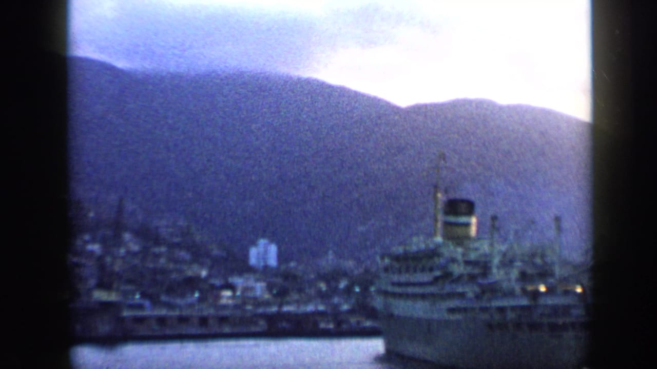 Hazy mountains above a coastal town and harbor with a large docked ship.