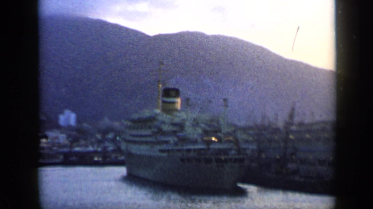 A docked passenger ship sits in a Venezuelan harbor beneath dark mountain slopes in this 1959 8mm frame.