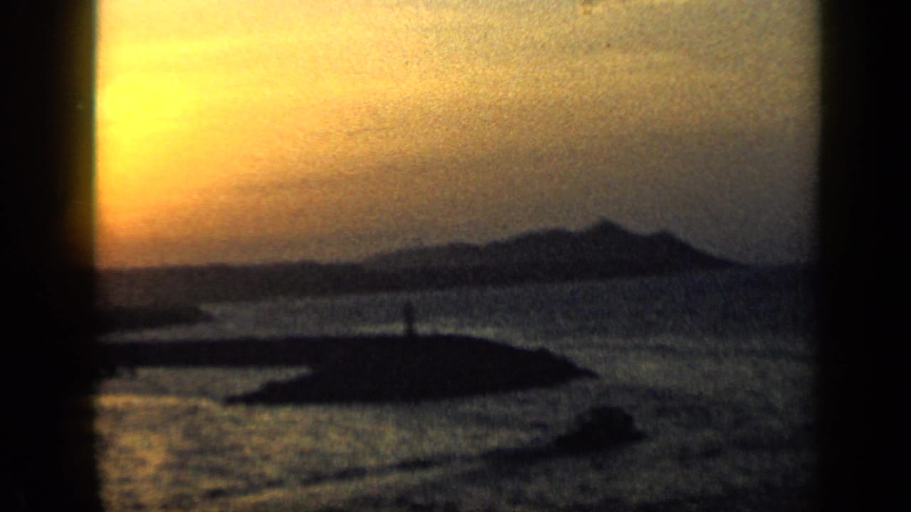 1959 Venezuela coastal harbor view at dusk, with water, a dark foreground landform, and distant hills under a fading sky.