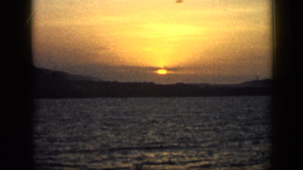 1959 Venezuela 8mm view of sunset light spreading through clouds above water and a distant mountain line.